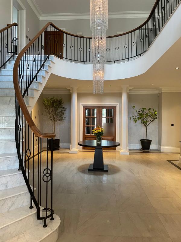 Crestron home automation in a Buckinghamshire house: the entrance hall, with a curved marble staircase, an iron balustrade and a tall crystal chandelier