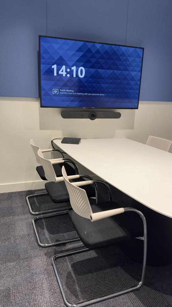 A meeting room video bar from Logitech mounted under the screen, looking out over a white table ringed by white chairs