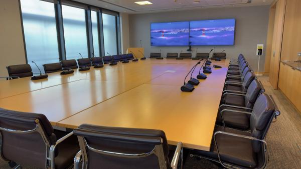 A boardroom audio system with microphone units running down both sides of a long timber table, and the Zoom Rooms start screen on the twin displays