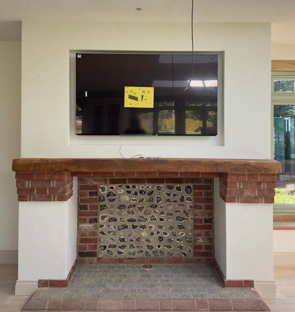 TV installation in Hampshire: a TV set into a recess above an oak beam mantel, with a brick and flint fireplace below