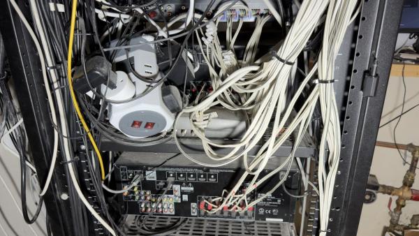 Control4 rescue, day one: behind a crowded rack, a stack of plug adaptors and a power strip sit over an AV receiver while thick white cable runs down the side to its speaker outputs
