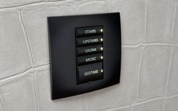 Five backlit buttons on a black wall keypad read stairs, upstairs, sauna, music and bedtime, in the house going from Control4 to Crestron Home