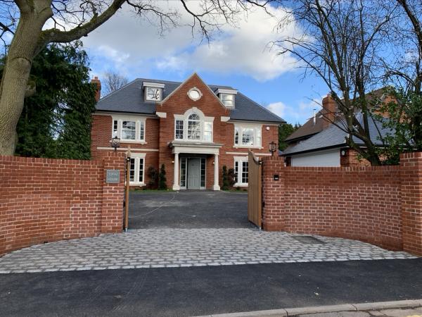 Red brick house seen from the road, behind a brick wall and gates