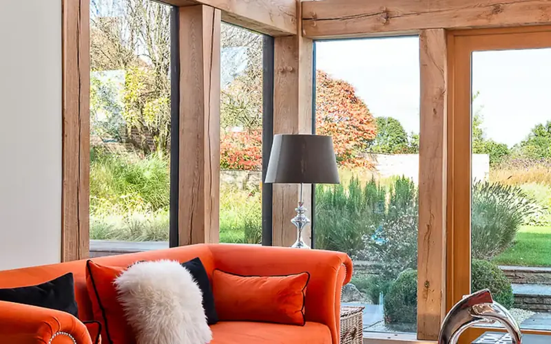 Living room with an orange sofa and tall oak framed doors opening onto the garden