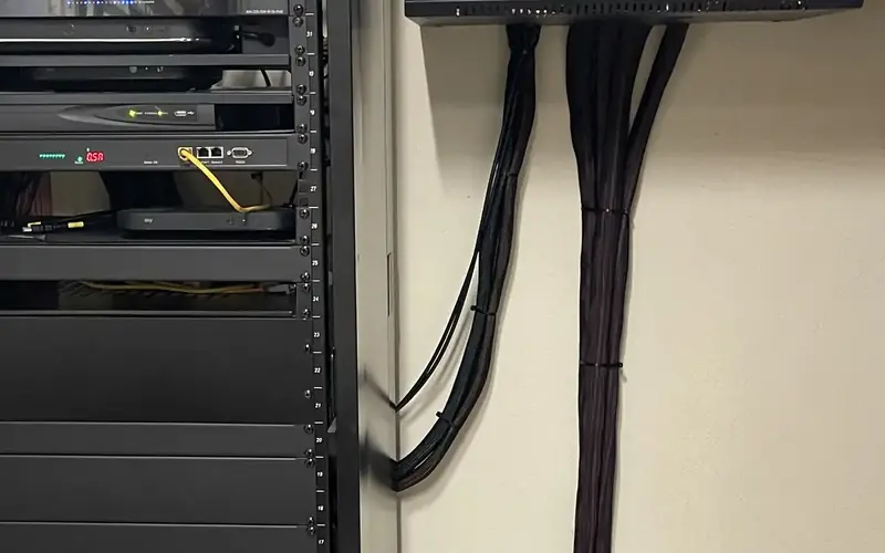 AV equipment rack beside black cable looms bundled neatly up a cream wall