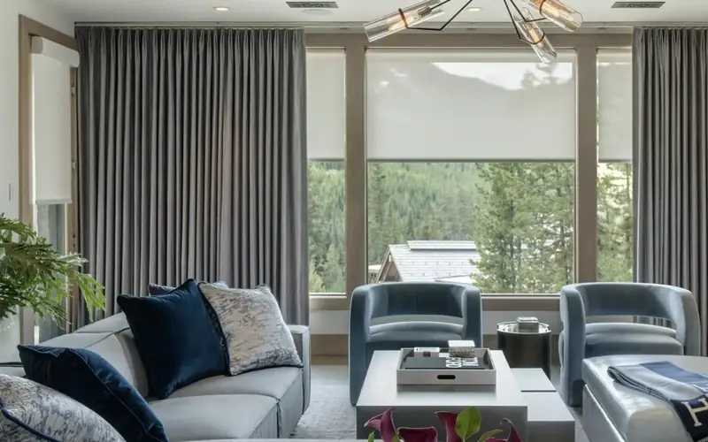 Living room with floor length grey curtains, a pale sofa with navy cushions and two blue armchairs
