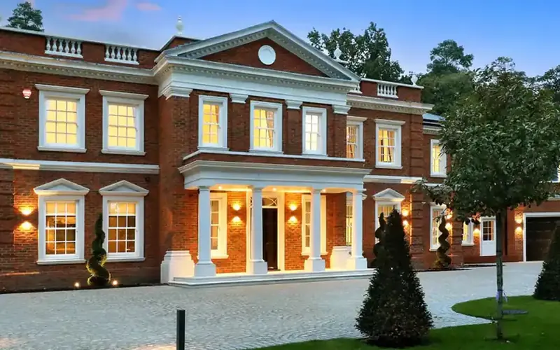 Red brick house with a white columned porch and lit windows at dusk
