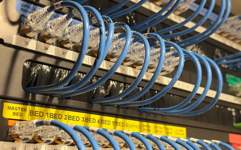Blue patch leads looped over a patch panel with yellow labels naming each room