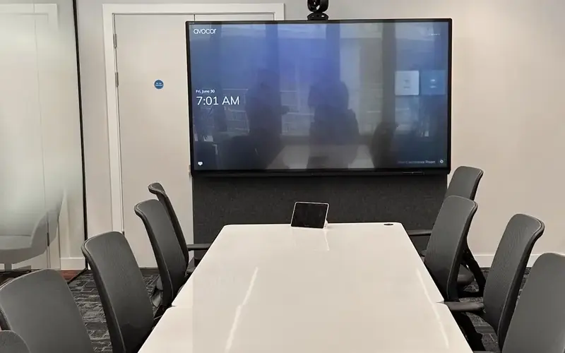 Meeting room with a large video conferencing screen and a white table